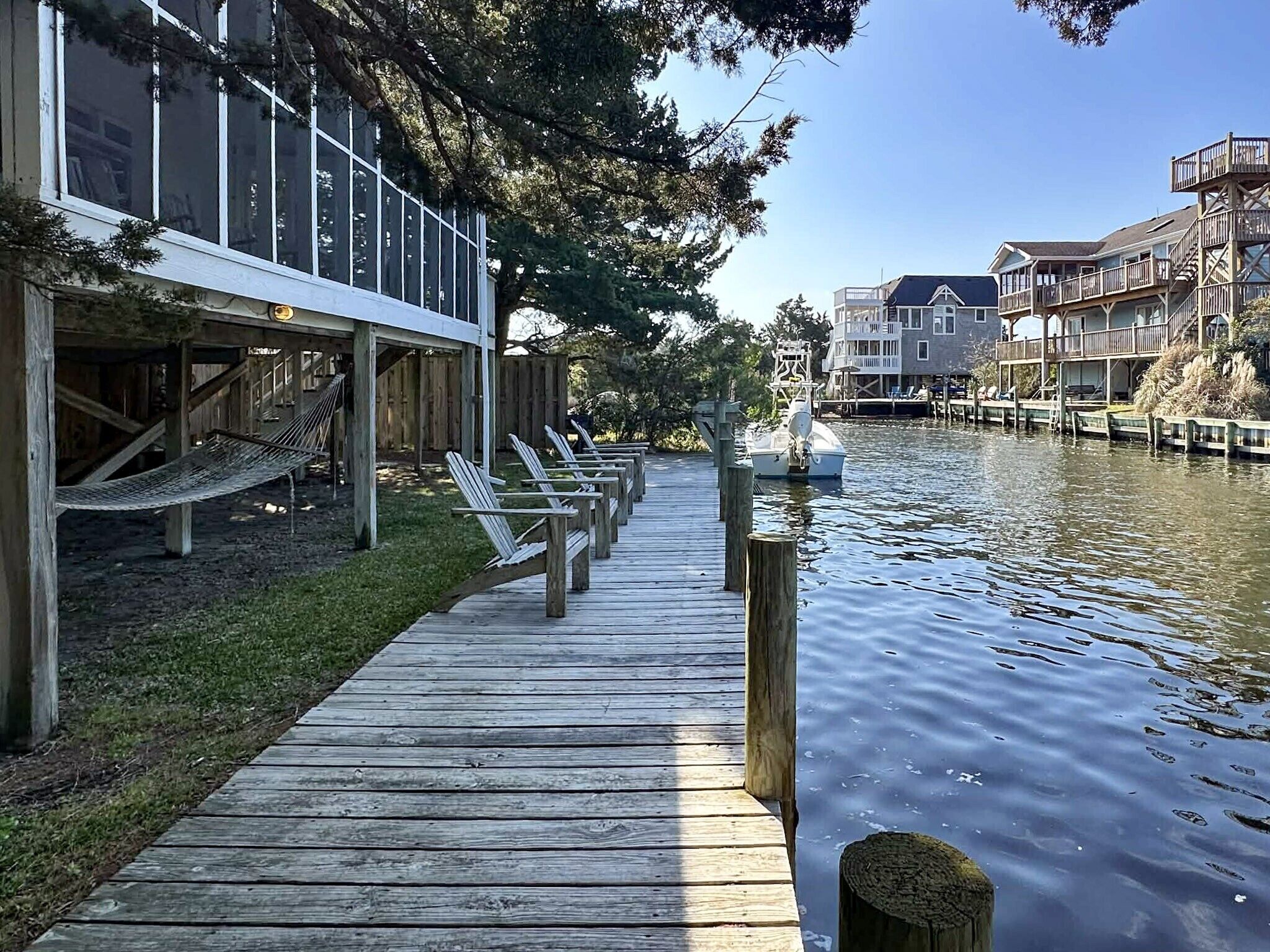 Un muelle de madera que conduce a un edificio con amplias ventanas, una embarcación amarrada cerca y una masa de agua tranquila.
