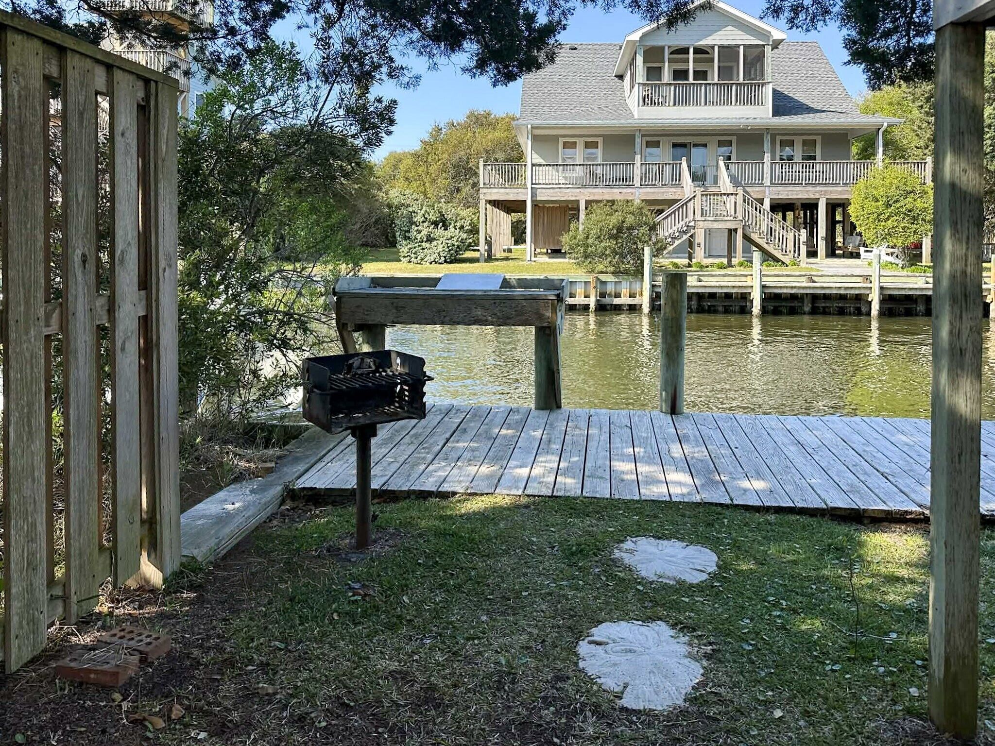 Une jetée en bois menant à une maison dotée d’un balcon, d’un barbecue et d’un étang.