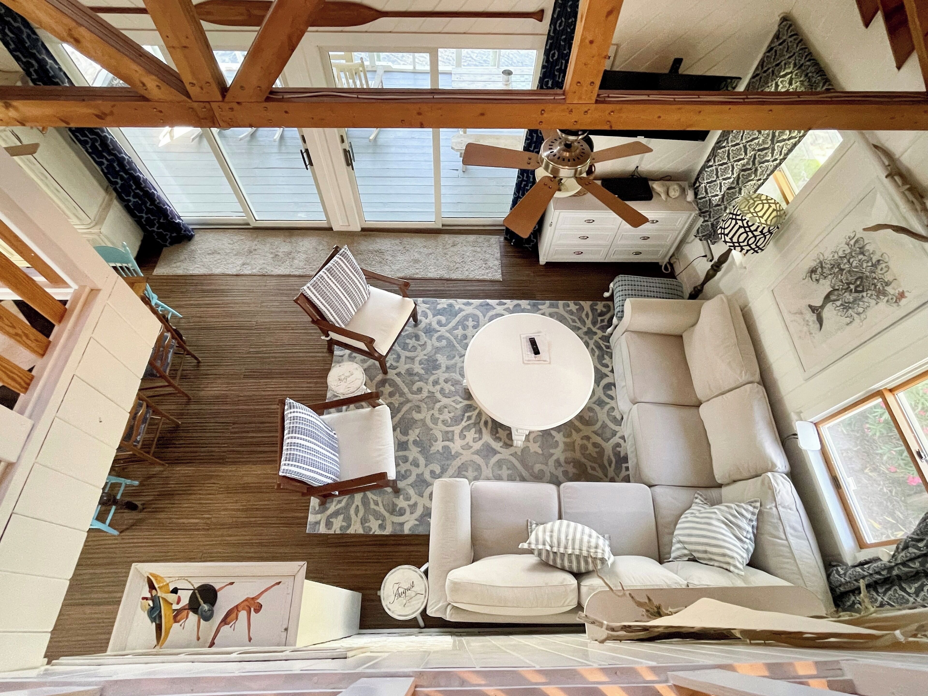A spacious living area with a high ceiling, wooden beams, a ceiling fan, a patterned rug, a white sofa, and a round coffee table.