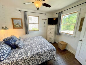A bedroom with a bed, a dresser, a television, and two windows.