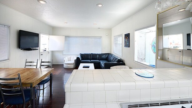 A modern hotel room with a wooden dining table, a black leather sofa, a white sofa, and a large mirror. - 319CE: Budget-friendly Cottage, 2.5 Blocks to Beach and Shops + WIFI (Avalon)