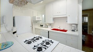 A kitchen with white cabinets, a red sink, a gas stove, a microwave, and a ceiling light fixture. - 319CE: Budget-friendly Cottage, 2.5 Blocks to Beach and Shops + WIFI (Avalon)