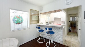 A modern kitchen with white cabinetry, a bar area with blue bar stools, and a round clock on the wall. - 319CE: Budget-friendly Cottage, 2.5 Blocks to Beach and Shops + WIFI (Avalon)