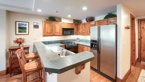 A kitchen with wooden cabinets, a stainless steel refrigerator, and a bar area with stools.