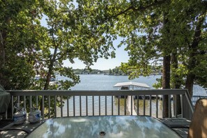A lakeside deck with a view of the water, trees, and a covered area.