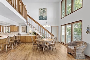 A spacious kitchen with a wooden staircase, a dining area with chairs, and large windows.