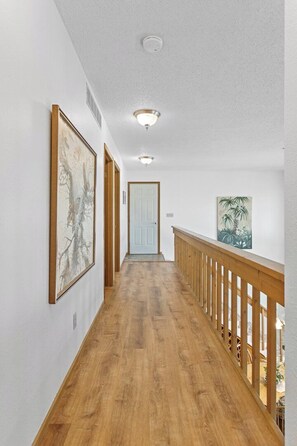 A hallway with wooden flooring, white walls, and a wooden railing.