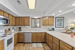 A modern kitchen with wooden cabinets, a stainless steel microwave, a dishwasher, and a large window.