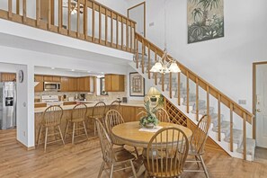 A spacious kitchen with wooden cabinets, a dining area with a round table and chairs, and a staircase with wooden railings.