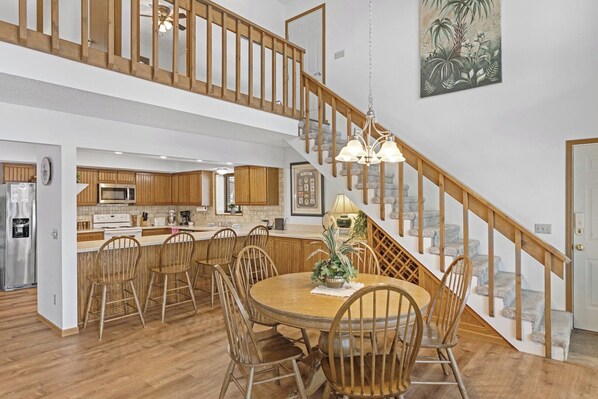 A spacious kitchen with wooden cabinets, a dining area with a round table and chairs, and a staircase with wooden railings.