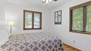 Ein Schlafzimmer mit einem Bett, Deckenventilator, zwei Fenstern mit Jalousien und einer Nachttischlampe.