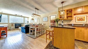 Amplia sala de estar con chimenea, mesa de comedor y cocina con armarios de madera y encimeras de granito.