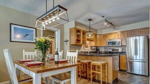 Una cocina moderna con armarios de madera, electrodomésticos de acero inoxidable y un comedor con mesa de madera y sillas blancas.