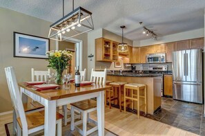 A modern kitchen with wooden cabinets, stainless steel appliances, and a dining area with a wooden table and white chairs.