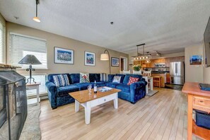 Sala de estar con sofá azul, una mesa de centro de madera y una cocina al fondo.