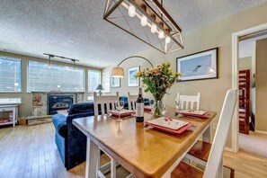 A dining area with a wooden table, chairs, a vase with flowers, and a fireplace. - Greystone Lodge 202 Ski-in/Out by Acer Vacations (Whistler)