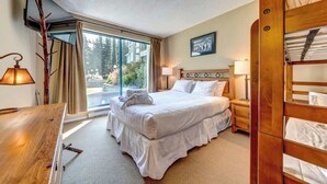 Habitación de hotel con cama, mesitas de noche, escritorio, silla, televisor y ventana con cortinas.