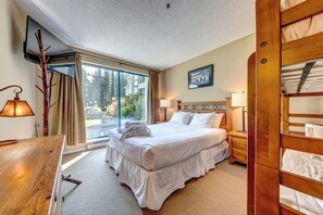 Ein Hotelzimmer mit Bett, Nachttischen, Schreibtisch, Stuhl, Fernseher und einem Fenster mit Vorhängen.