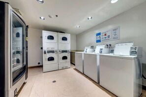 A laundry area with multiple washing machines and dryers, a glass-fronted vending machine, and a wall-mounted information board.