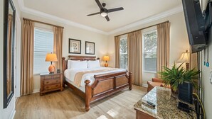 A hotel room with a wooden bed, two bedside tables with lamps, a ceiling fan, a television, and a large window with curtains. - Patriot's Eden: Golf, Water Park, Near Disney (Kissimmee)