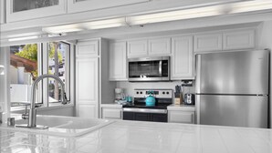 A modern kitchen with white cabinetry, stainless steel appliances, and a large window providing natural light. - H962: Great Ocean Views, Golf Cart + Only 10 Steps + King Bed + Fireplace (Avalon)