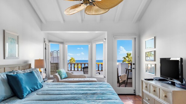 A bedroom with a bed, a TV, and a balcony with a view of the ocean. - H962: Great Ocean Views, Golf Cart + Only 10 Steps + King Bed + Fireplace (Avalon)