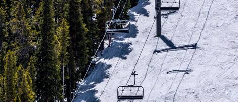 A ski lift with chairs moving up and down a snowy slope, surrounded by dense evergreen trees.