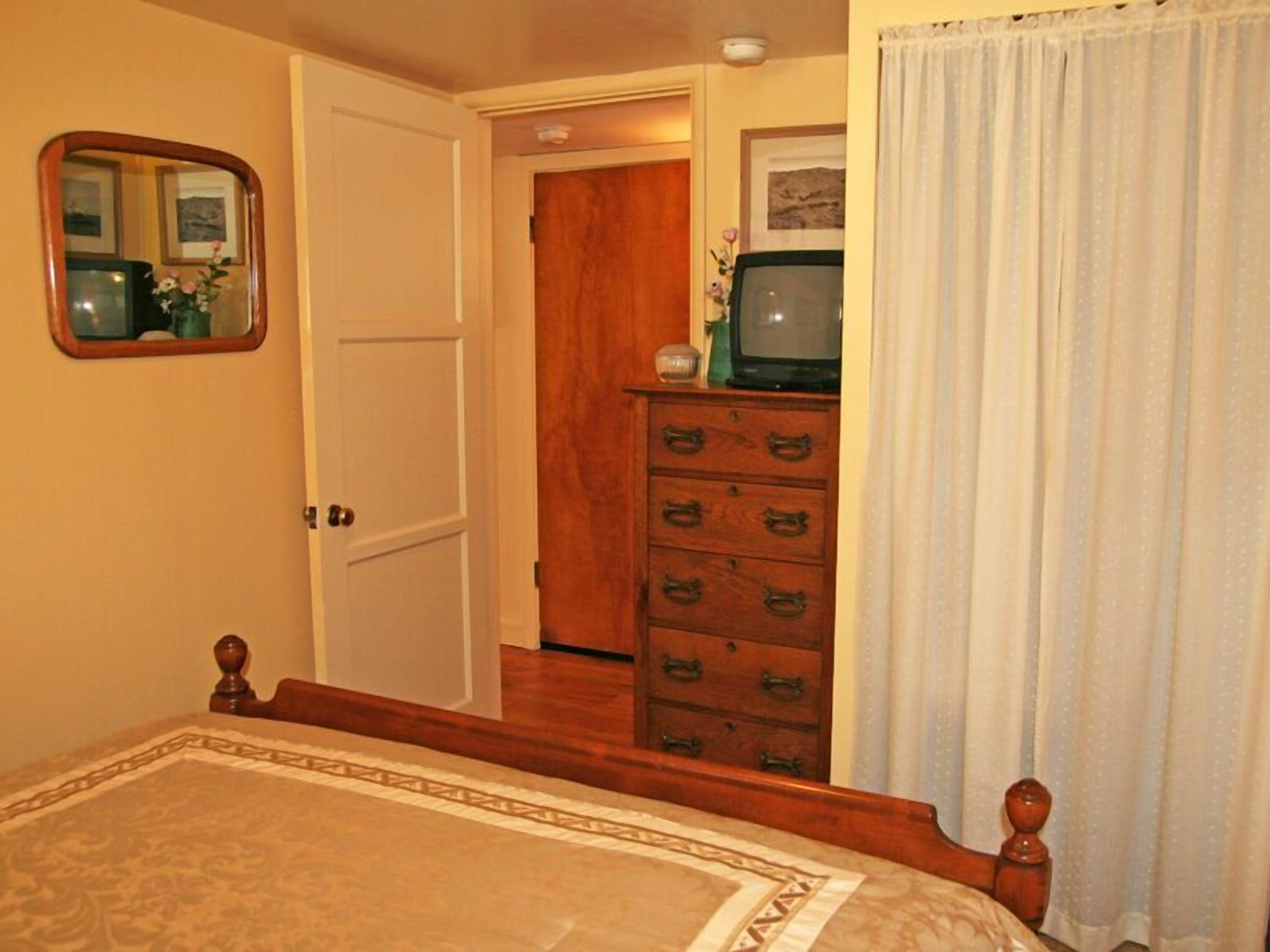 A bedroom with a bed, a dresser, a television, and a mirror.