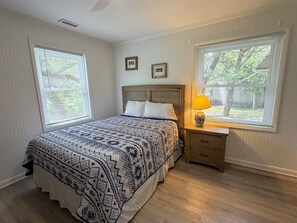 A bedroom with a bed, two windows, a nightstand, and a lamp.