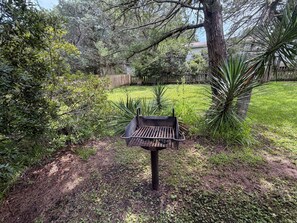 Un barbecue dans un jardin, avec une clôture en bois et des arbres.