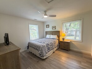A bedroom with a bed, a desk, a chair, a ceiling fan, and two windows with blinds.