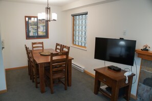 Un comedor con una mesa y sillas de madera, un televisor sobre un mueble bajo y un ventanal con vidrio esmerilado.
