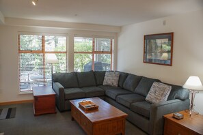 A living room with a sectional sofa, a wooden coffee table, a side table, and a lamp.