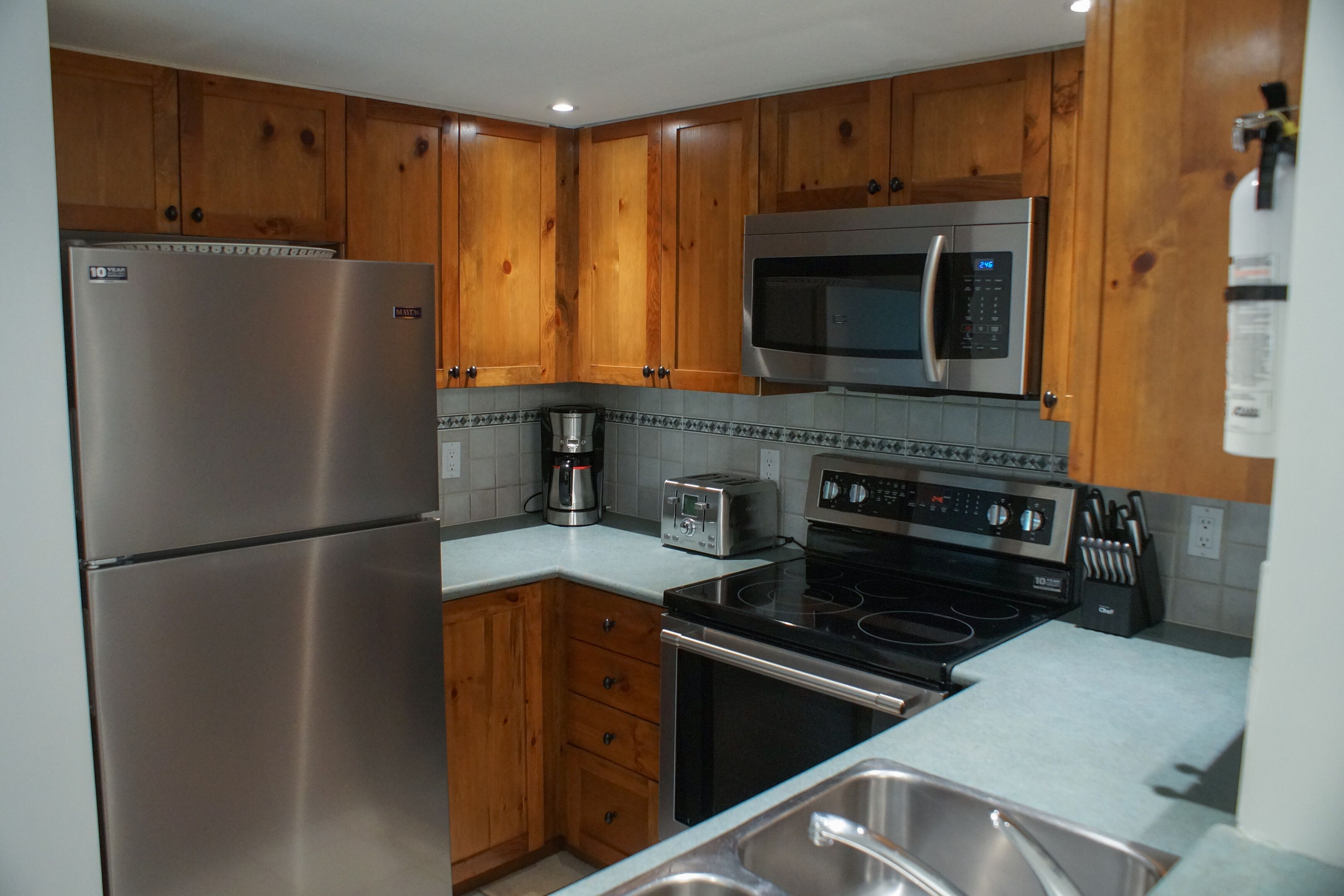 A kitchen with wooden cabinets, a stainless steel refrigerator, a microwave, a toaster, and an oven.