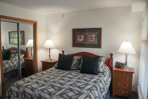 A bedroom with a bed, two bedside tables, a mirror, and two wall-mounted picture frames.