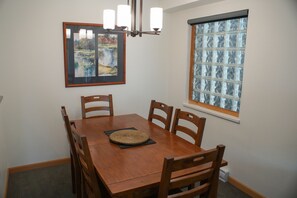 A dining area with a wooden table, four chairs, a framed painting, a chandelier, and a window with frosted glass. - Stoney Creek Northstar 2 (Whistler)