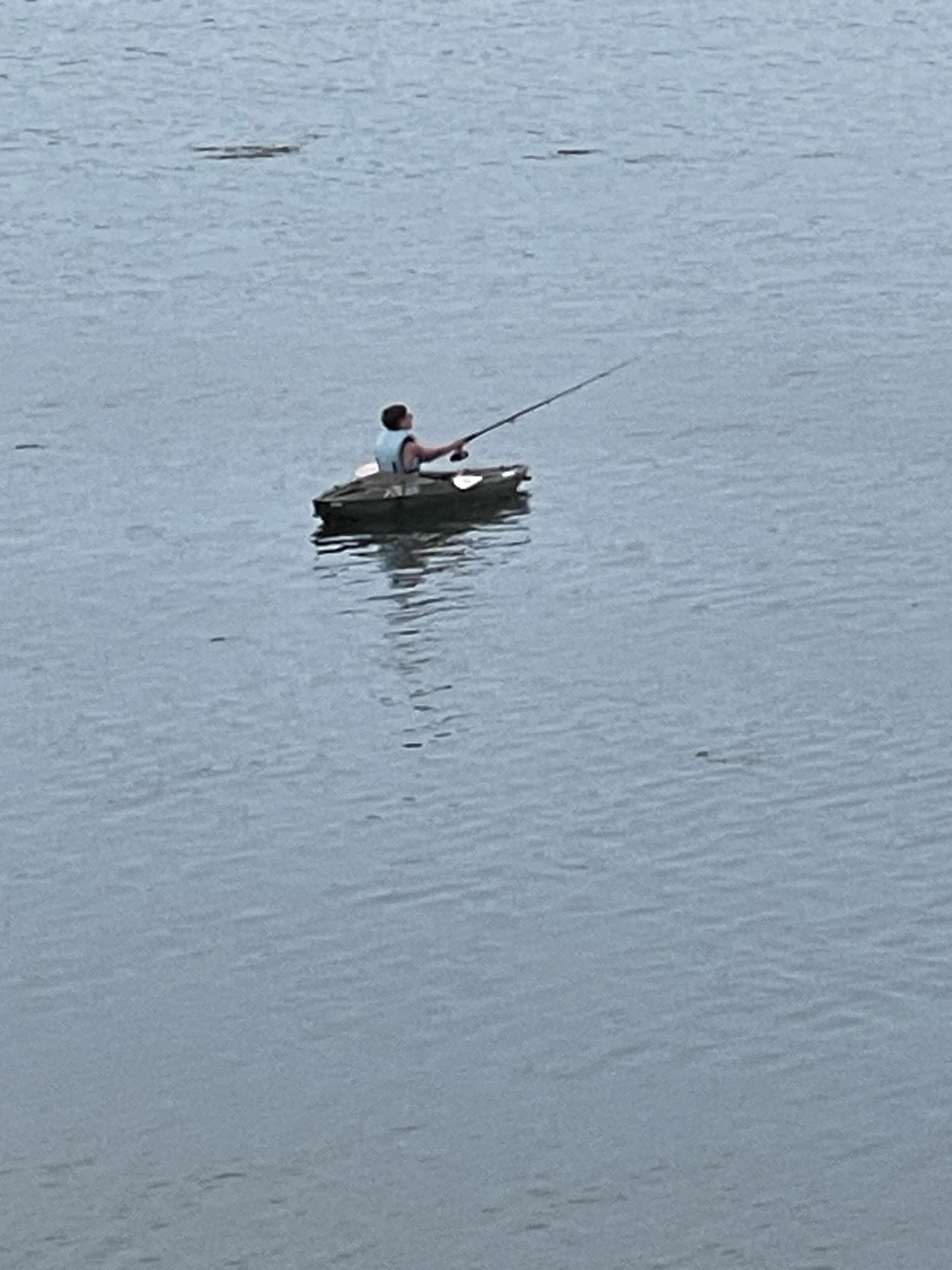 A person fishing from a small boat on calm water.