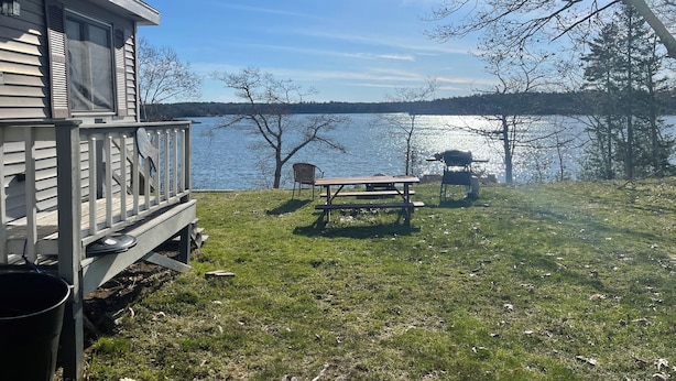 A lakeside property with a deck, picnic table, and barbecue grill. - Camp Forever cottage (Harpswell)