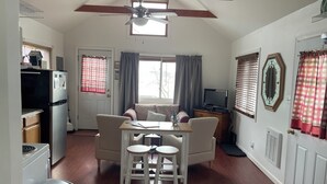 A compact living space with a kitchenette, a dining area with a table and chairs, a sofa, a ceiling fan, and a television. - Camp Forever cottage (Harpswell)