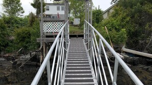 A metal staircase leading to a wooden deck over water, surrounded by greenery. - Camp Forever cottage (Harpswell)