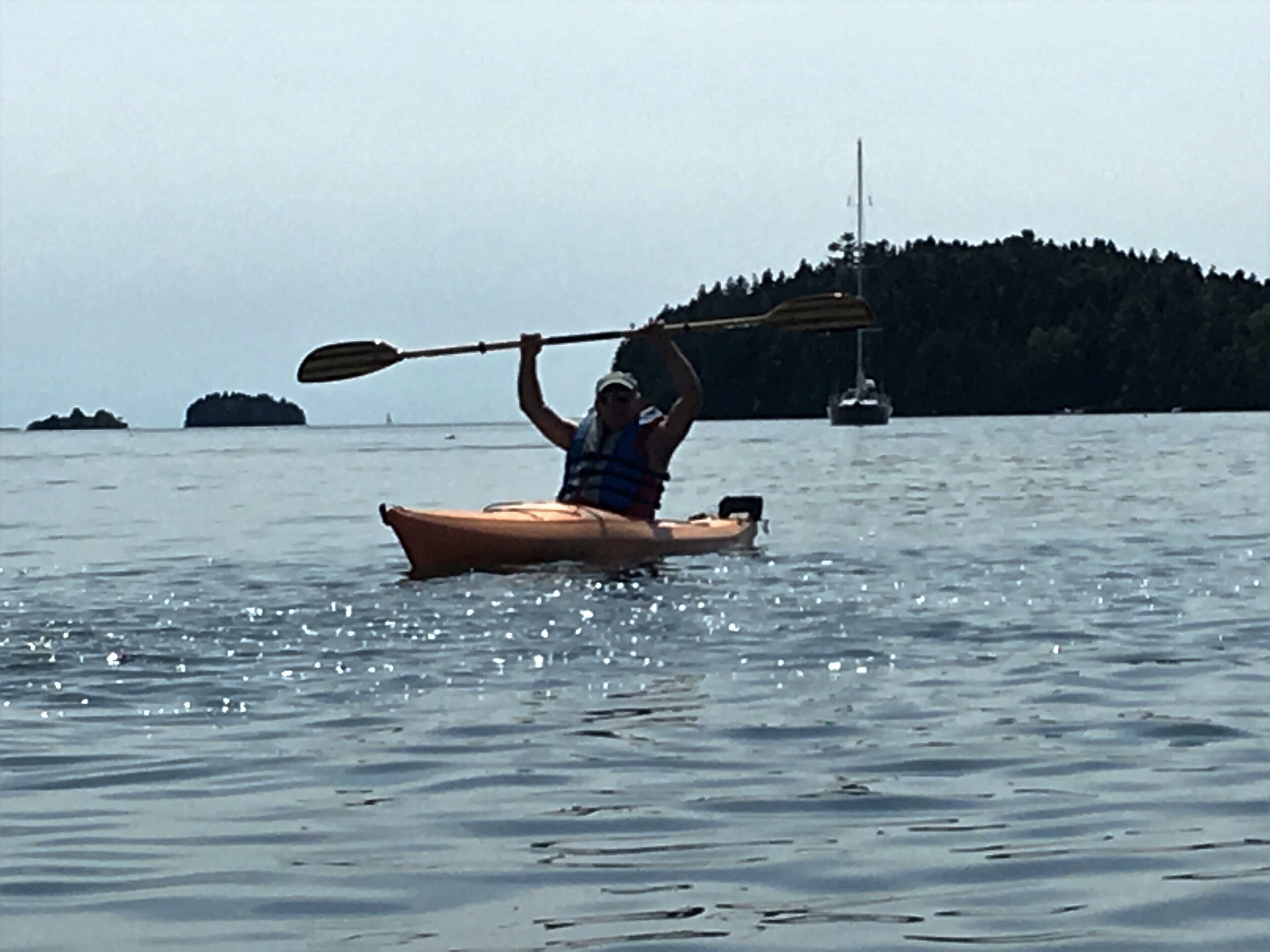 Une personne pratiquant le kayak sur une étendue d’eau calme, avec une île boisée en arrière-plan.