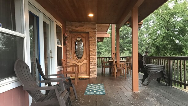 Una terraza de madera con mobiliario exterior, un muro de piedra y una puerta.