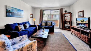 Ein Wohnzimmer mit blauem Sofagarnitur, einem Couchtisch, einem Bücherregal und einem Fernseher.