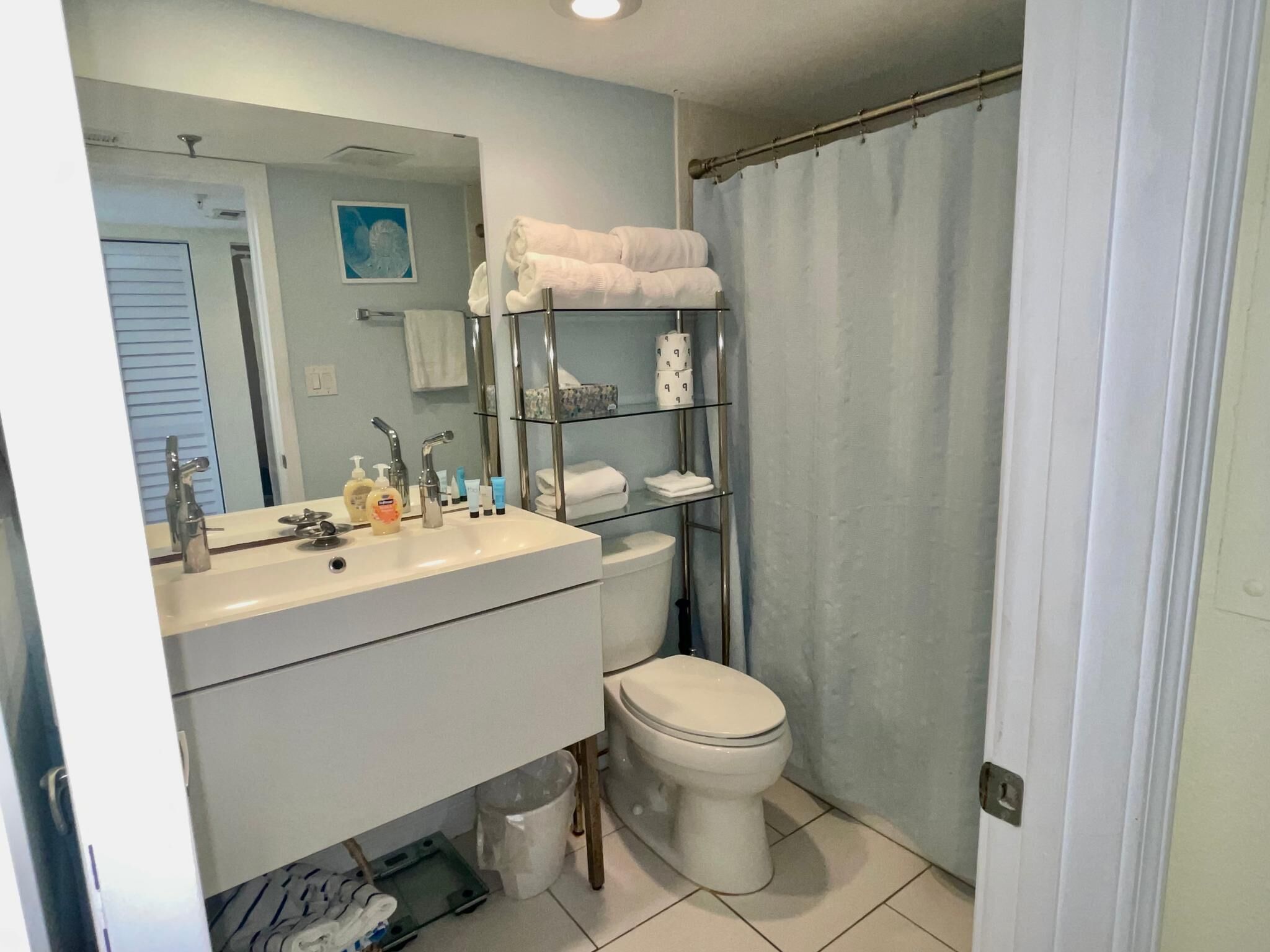 Een badkamer met een wit wastafelmeubel, spiegel en toilet. Er is een plank met toiletartikelen en handdoeken.