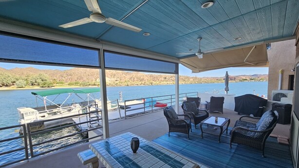 A covered outdoor deck with a pool table, chairs, and a view of a lake and mountains.