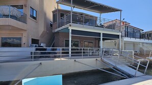 A waterfront property with a covered dock, a blue bench, and a building with multiple balconies and a staircase leading to an upper level.