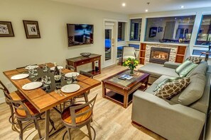 A dining area with a wooden table and chairs, a sofa, a fireplace, and a television mounted on the wall.