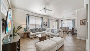 Un salon spacieux comprenant un canapé d’angle, une table basse en verre, un ventilateur de plafond et un coin repas avec des chaises et une table.