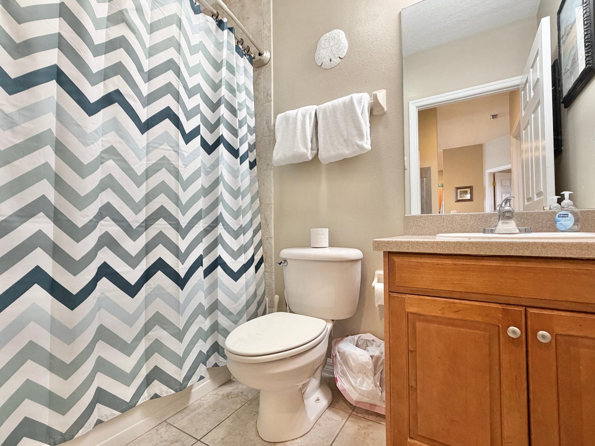Une salle de bain avec un rideau de douche à motifs en chevrons, des toilettes, un lavabo avec un miroir et un meuble en bois.