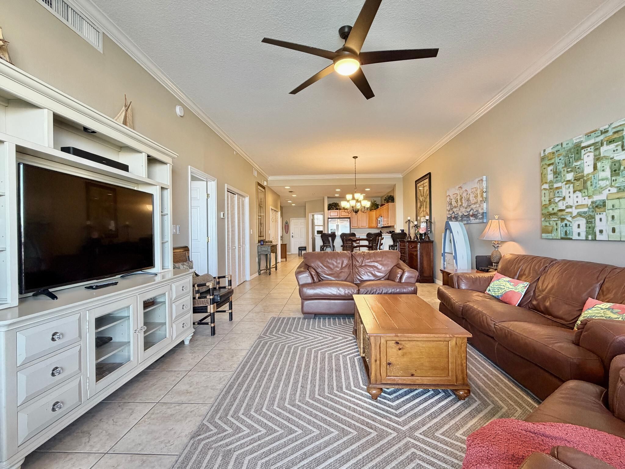 A living room with a television, leather sofas, a wooden coffee table, a patterned rug, and a ceiling fan.